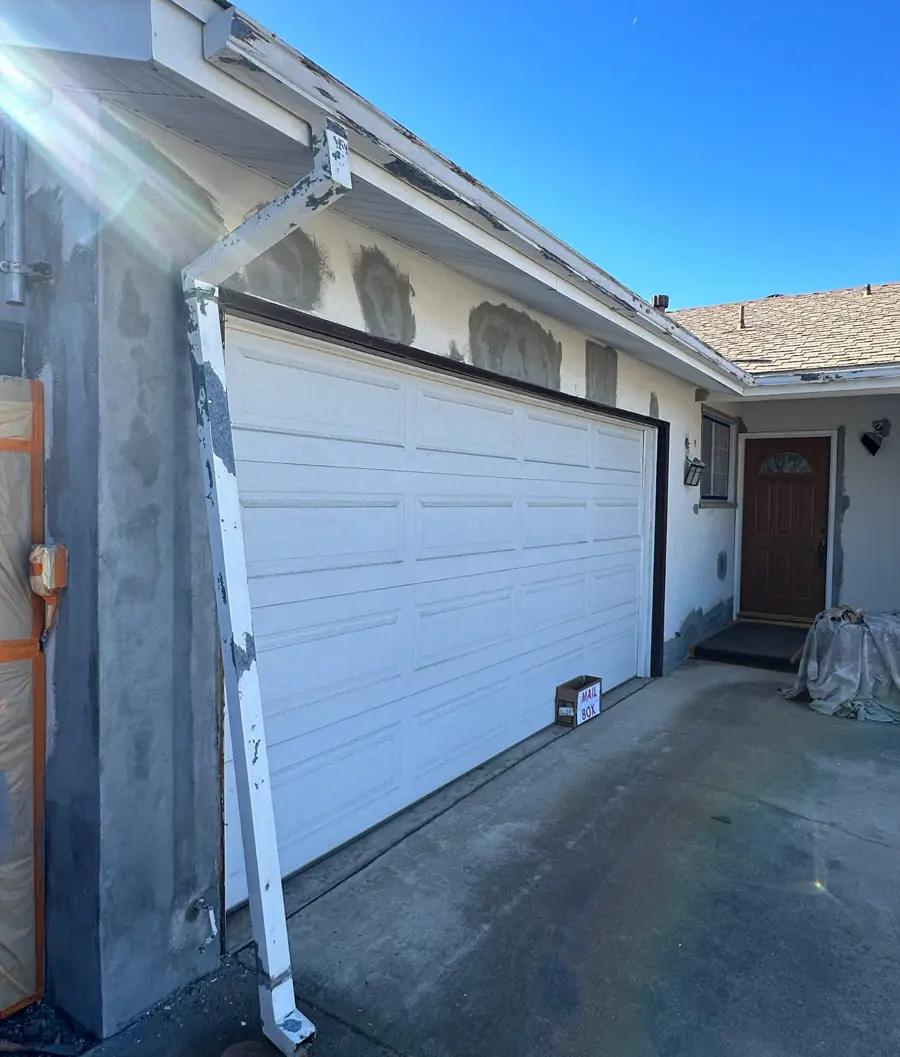 Before: the same garage wall with patched stucco, bare primer spots, and worn fascia