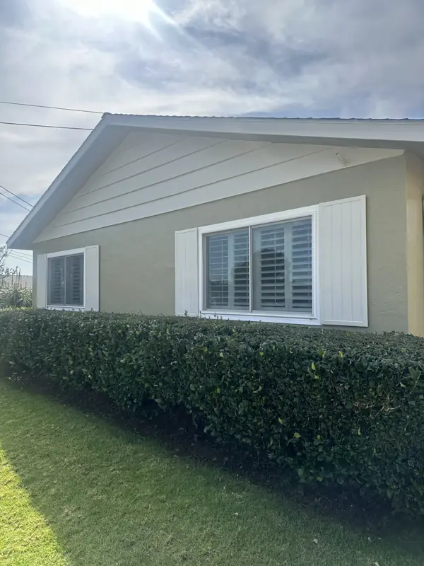 Single-story home with a warm greige exterior coating, white shutters, and a trimmed hedge