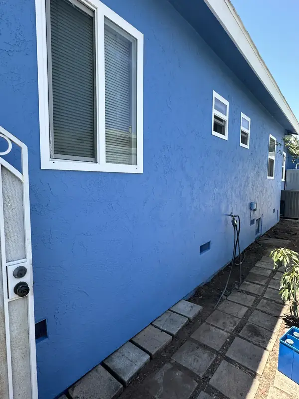 Side of a home finished in a bold blue exterior coating with crisp white window trim